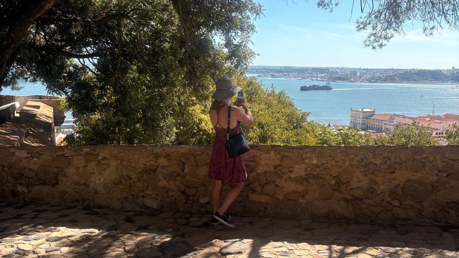A woman takes a photograph while walking around the ramparts above Lisbon