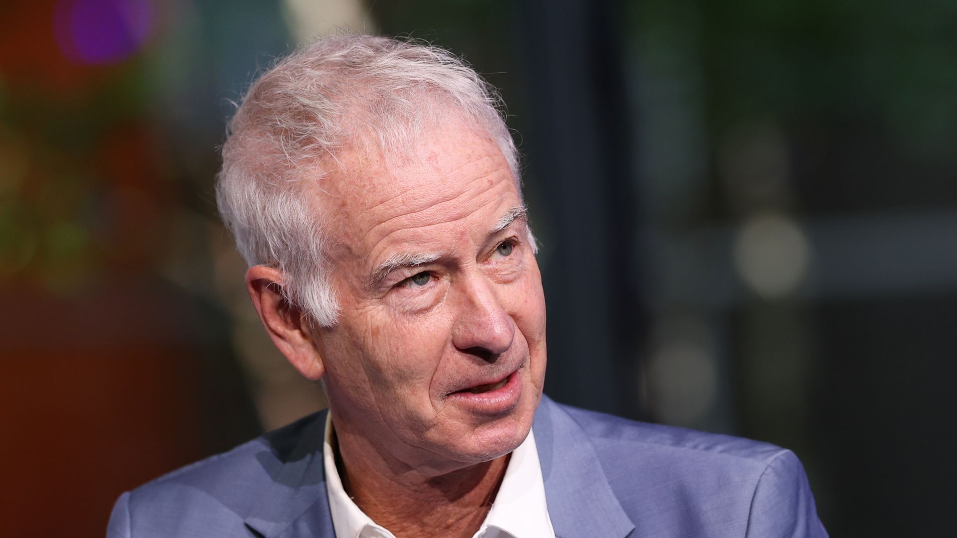 John McEnroe looking to right in white shirt and blue jacket