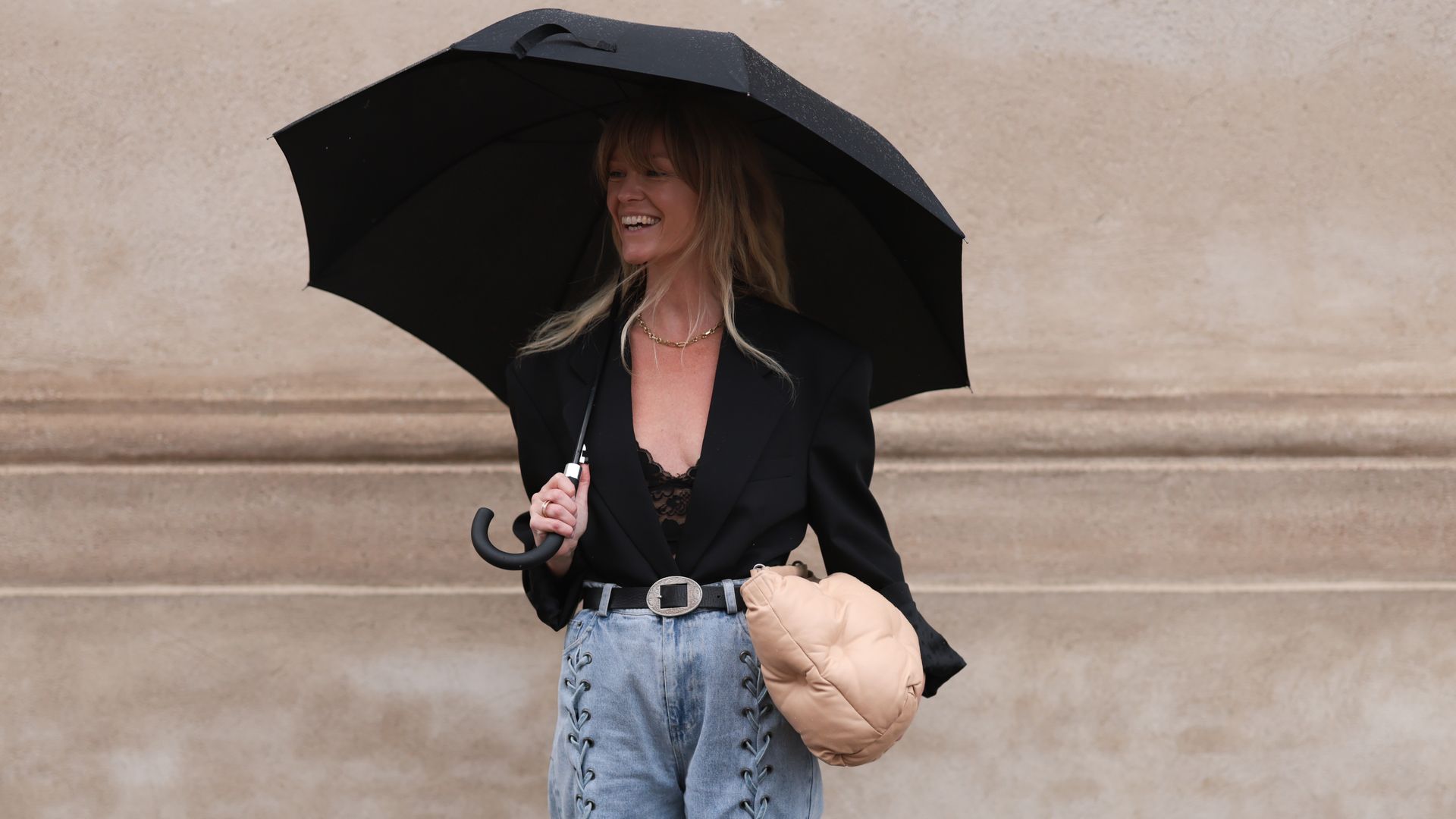 Jeanette Friis Madsen seen wearing black laced body top, black blazer jacket, light blue laced denim jeans pants, Maison Margiela beige leather pouch bag, black leather belt, black leather boots and  black umbrella, outside The Garment,