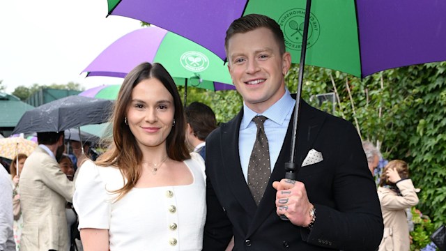 Holly Ramsay in a white dress and Adam Peaty in a black suit holding an umbrella