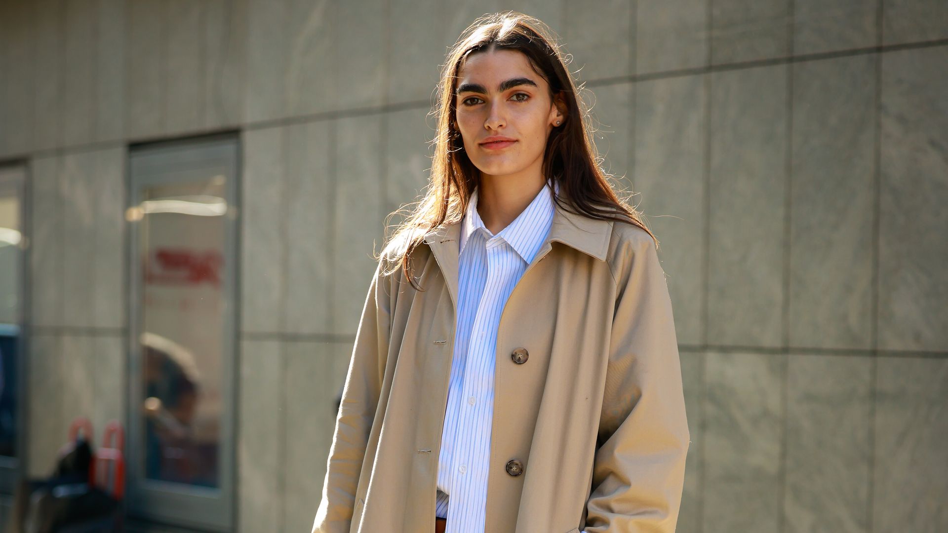 A guest wearing trench, white shirt, black wide pants and brown bag outside Mithridate during London Fashion Week 