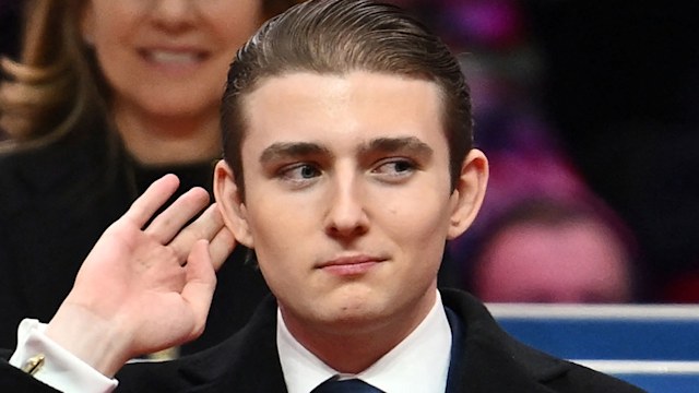 Barron Trump puts hand to ear with gesture wearing suit