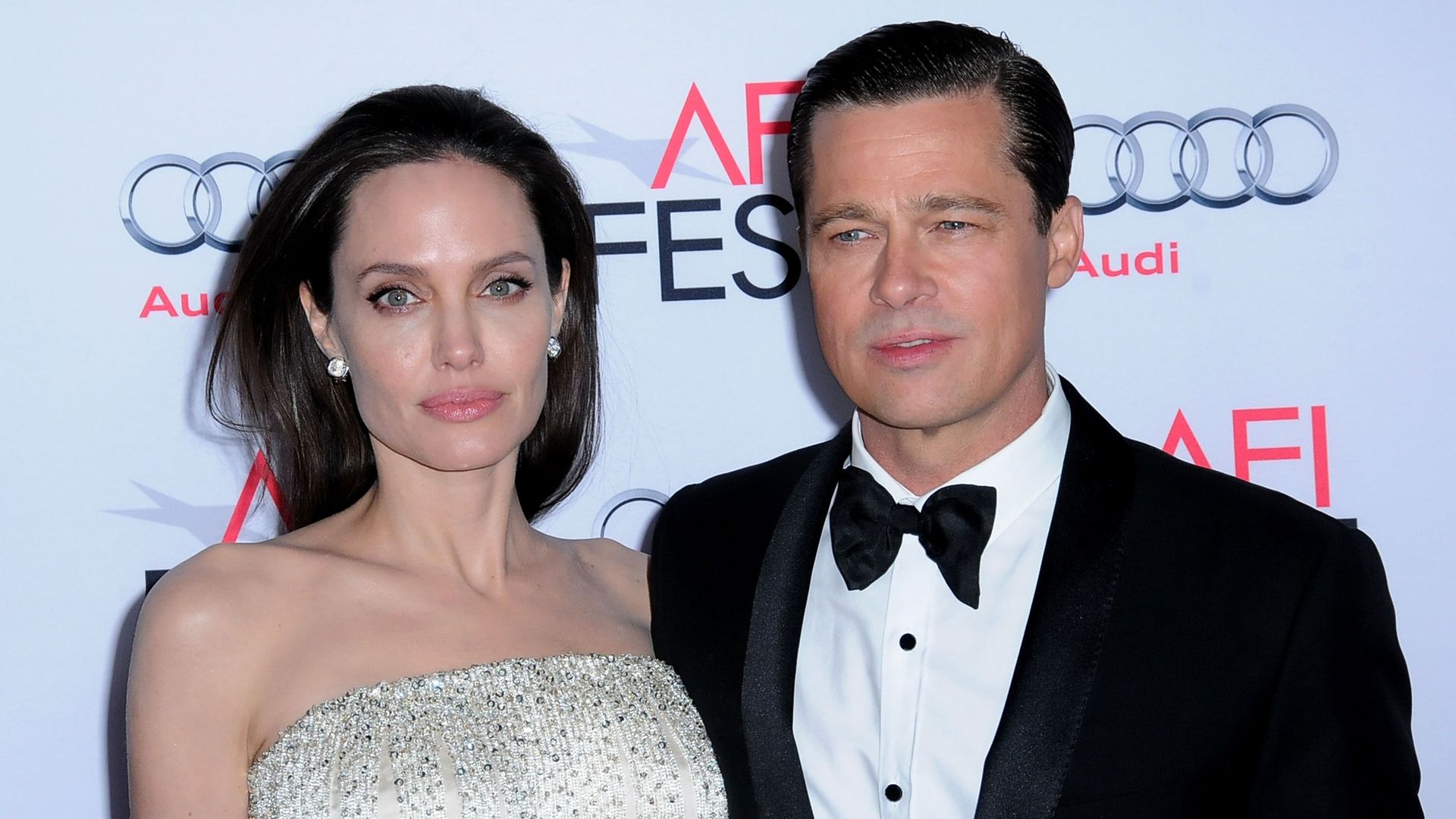 Angelina posing in a sparkly white dress with her arm around Brad Pitt in a bow and tie suit