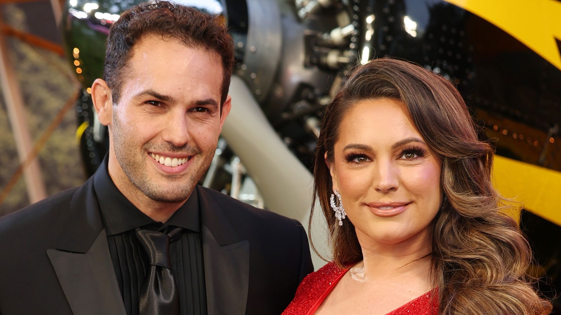 Jeremy Parisi and Kelly Brook in red dress in front of mock helicopter