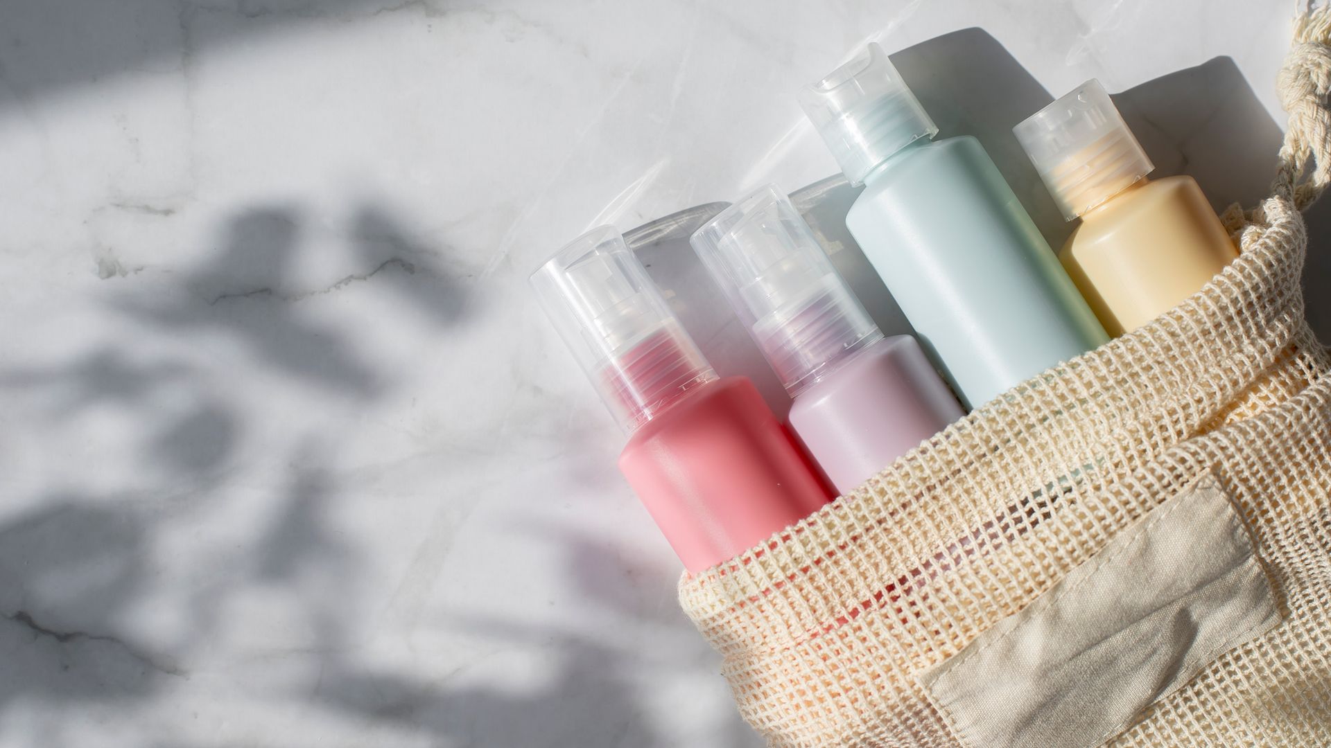 Small pastel colors bottles for travelling on white marble background. Copy space. Flat lay composition of cosmetic products. Top view