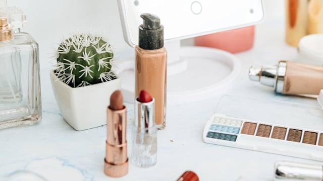 Pile of various cosmetics, make-up lie on wooden dressing table