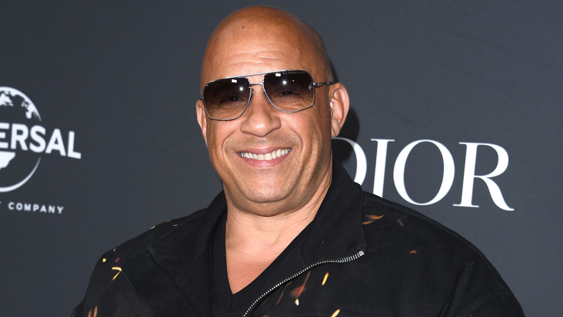 Vin Diesel smiling for a red carpet photo wearing sunglasses