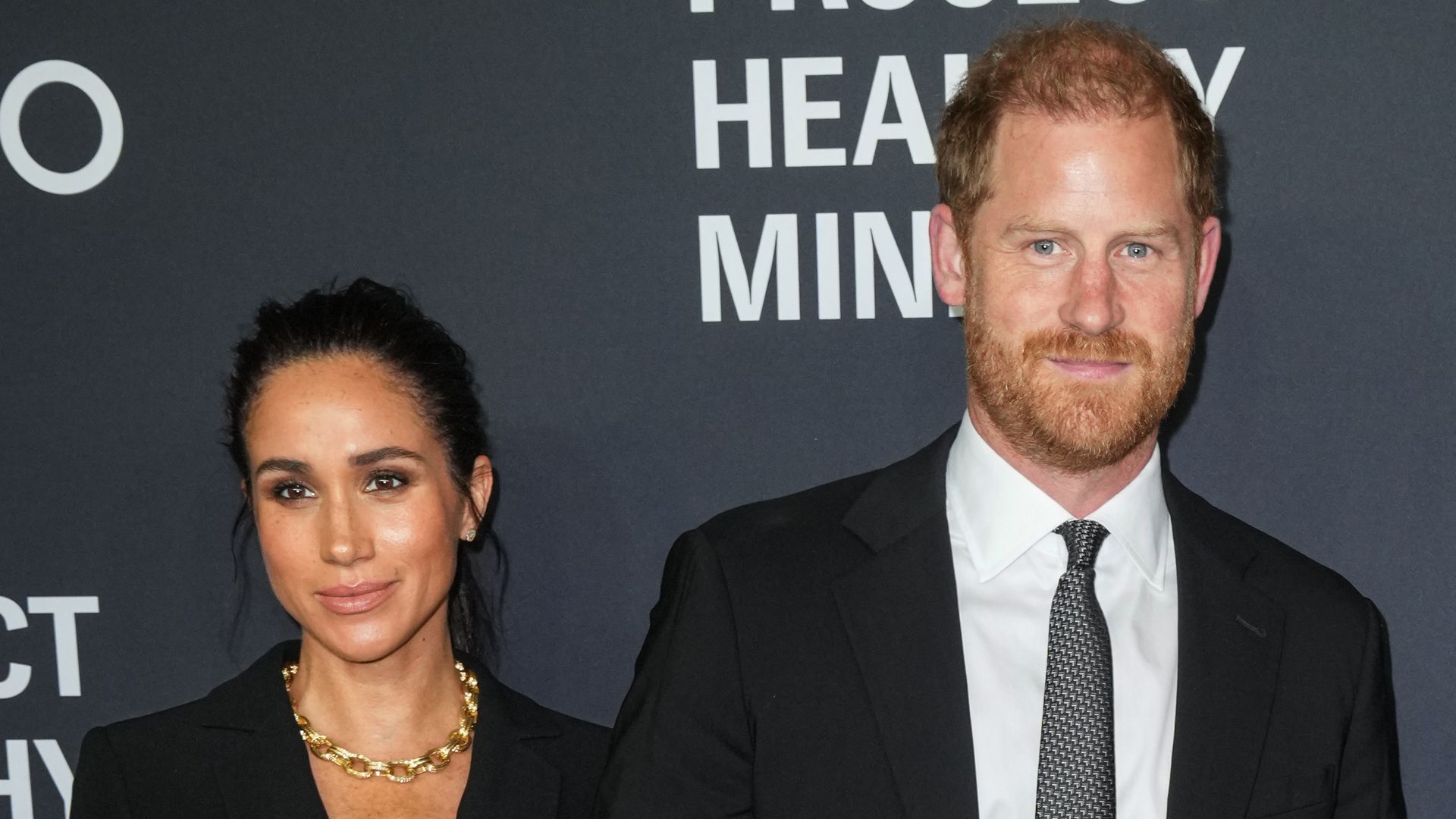 Meghan, Duchess of Sussex in black suit and Prince Harry in suit posed together