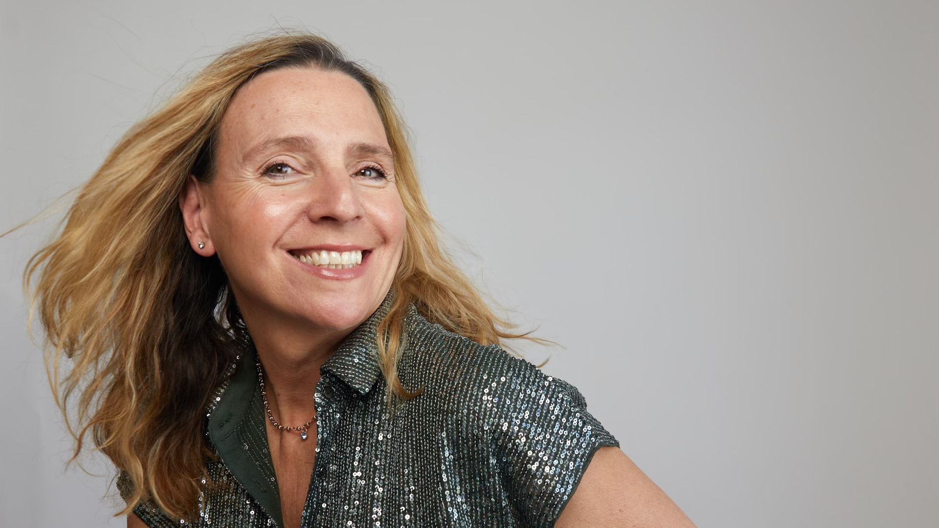Woman smiling in a glitter top and white jeans