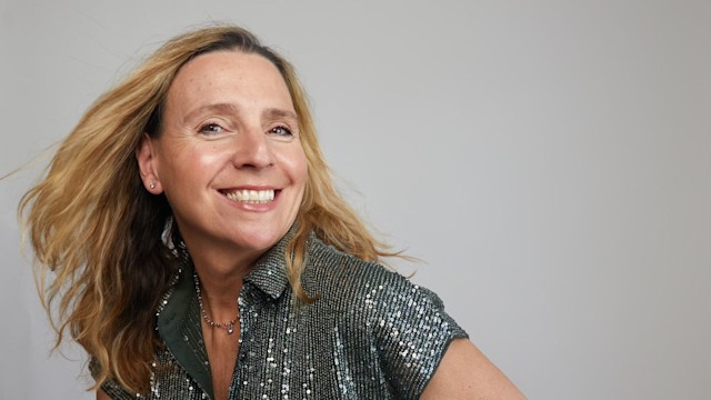 Woman smiling in a glitter top and white jeans 