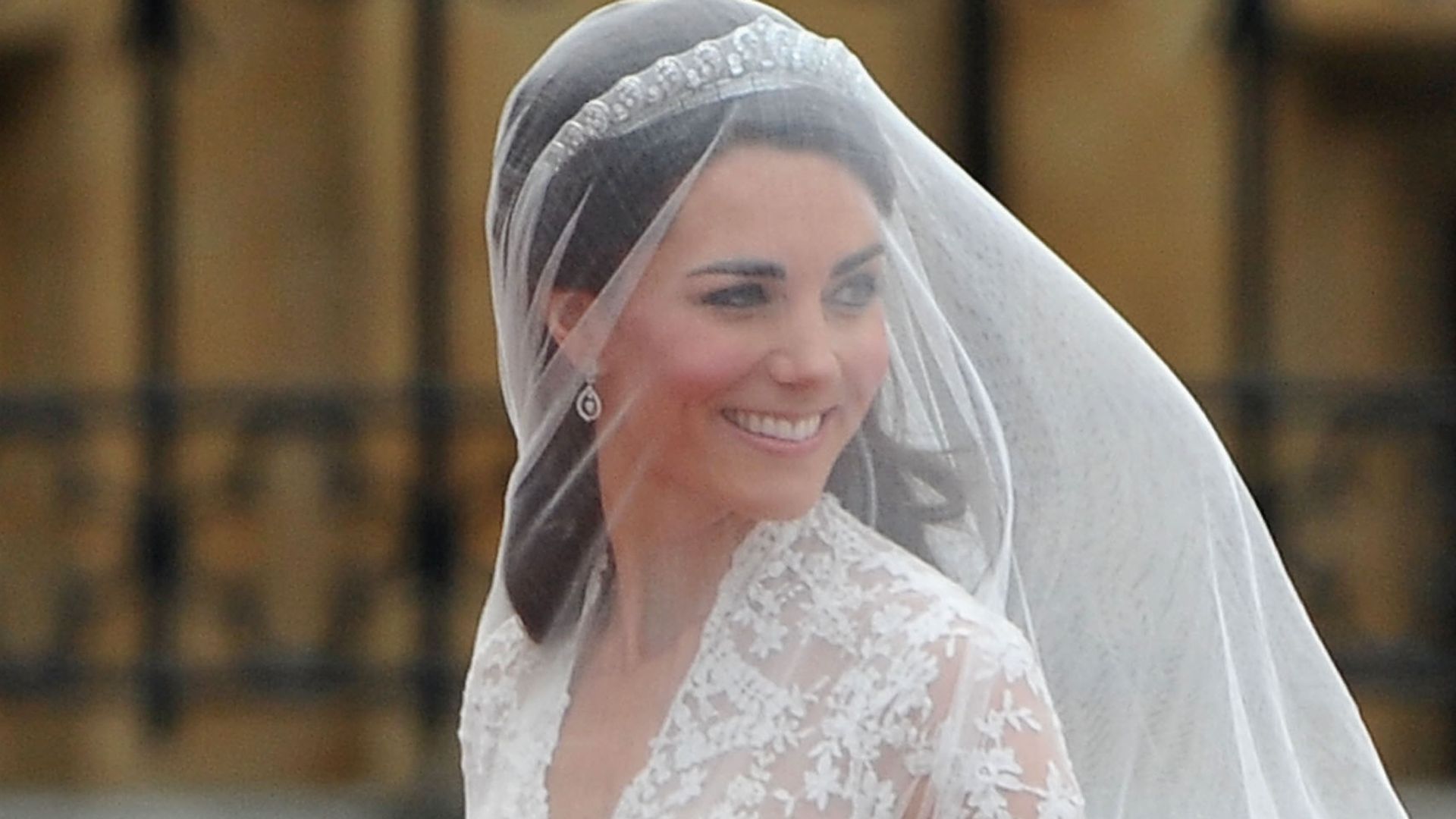 Kate Middleton wearing a veil and a wedding dress looking over her shoulders