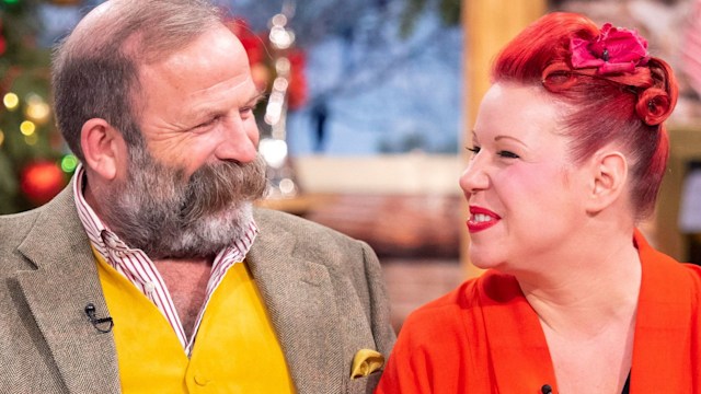 Dick Strawbridge in a yellow waistcoat on the sofa with Angel in a red coat