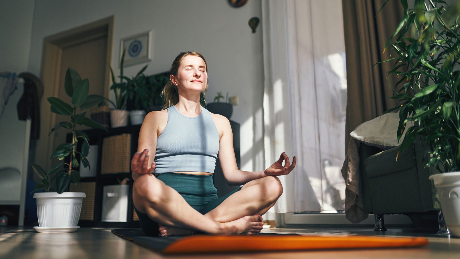 woman meditating in her living space, evoking a sense of harmony and inner peace. Her relaxed posture in the light-filled room illustrates a deep connection with her yoga journey.