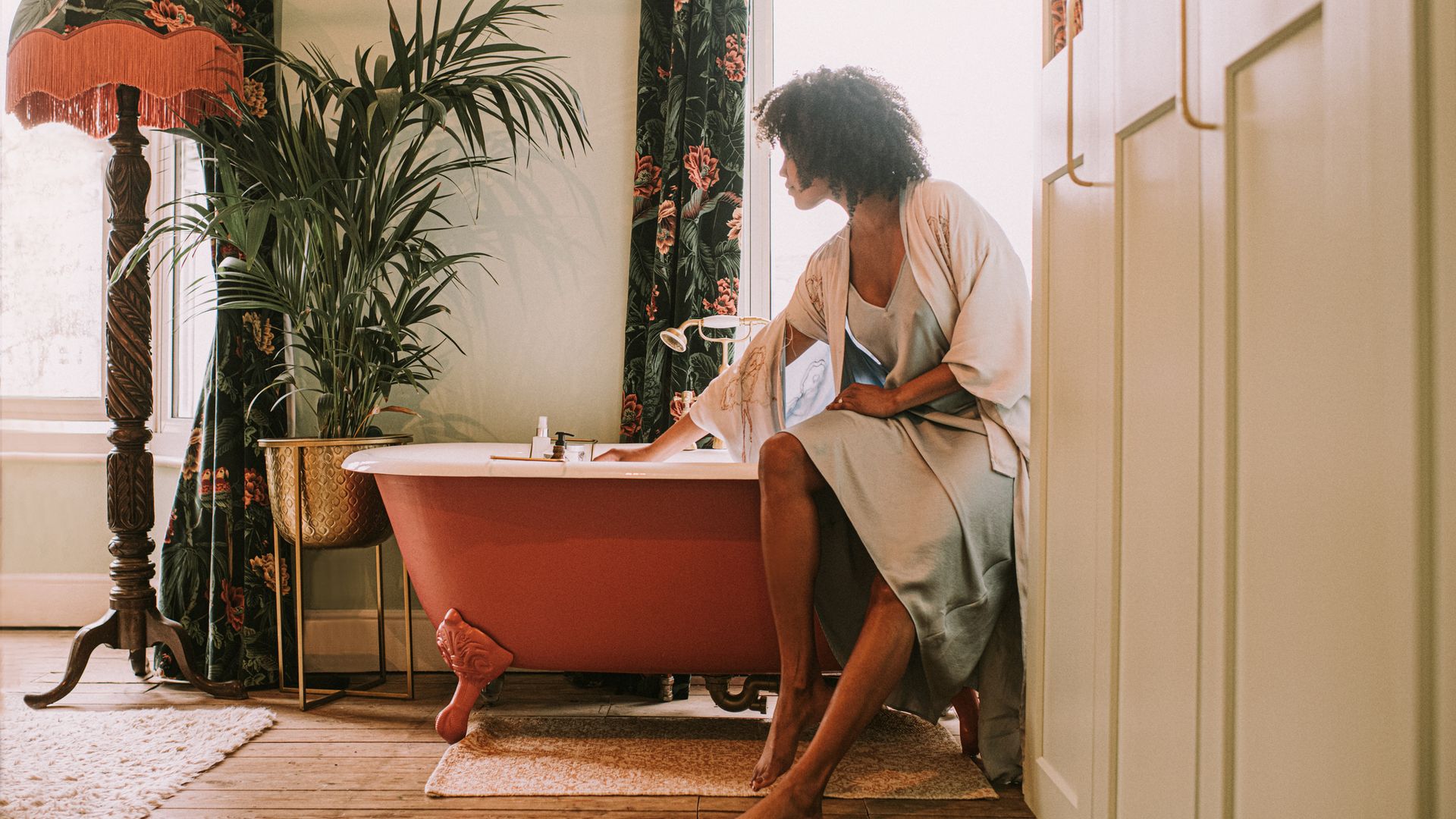 A woman perches on the side of an elegant red roll top bathtub.