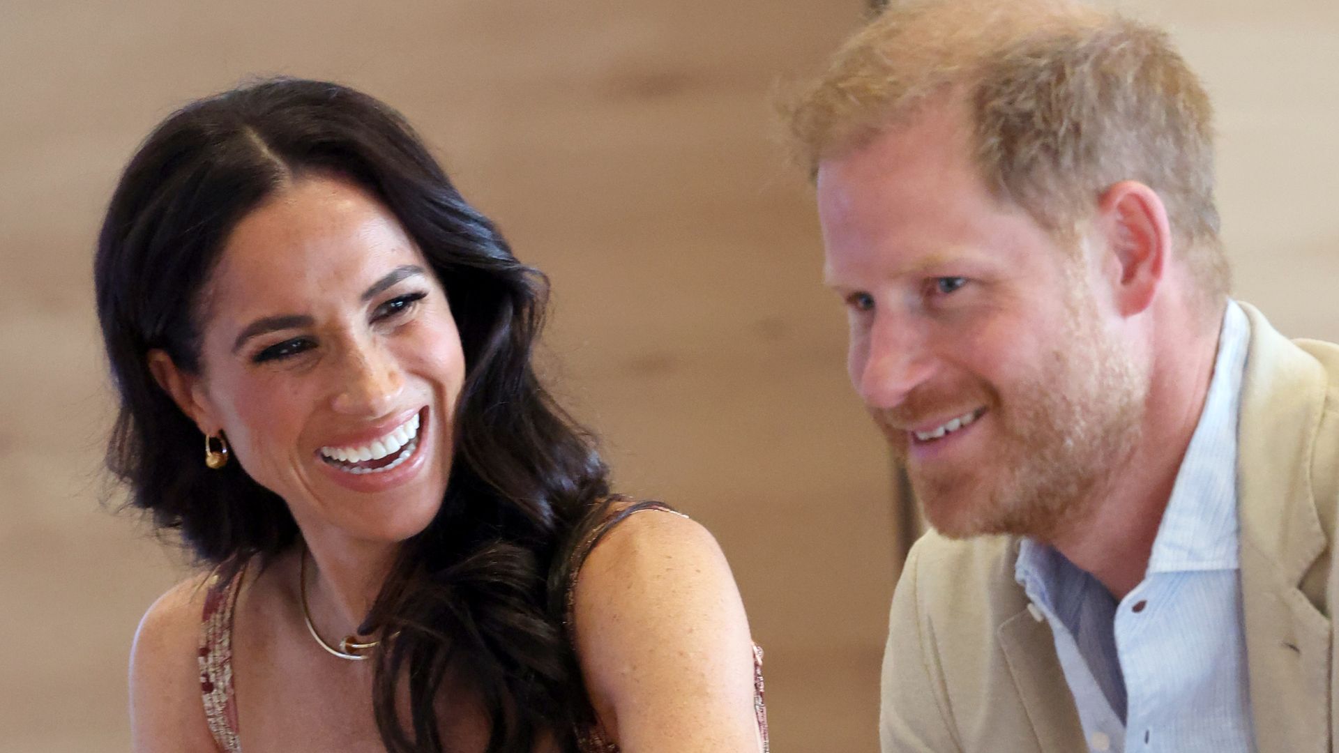 Meghan Markle in a red sundress laughing at Prince Harry
