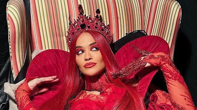 Rita Ora sat in a chair wearing a red costume