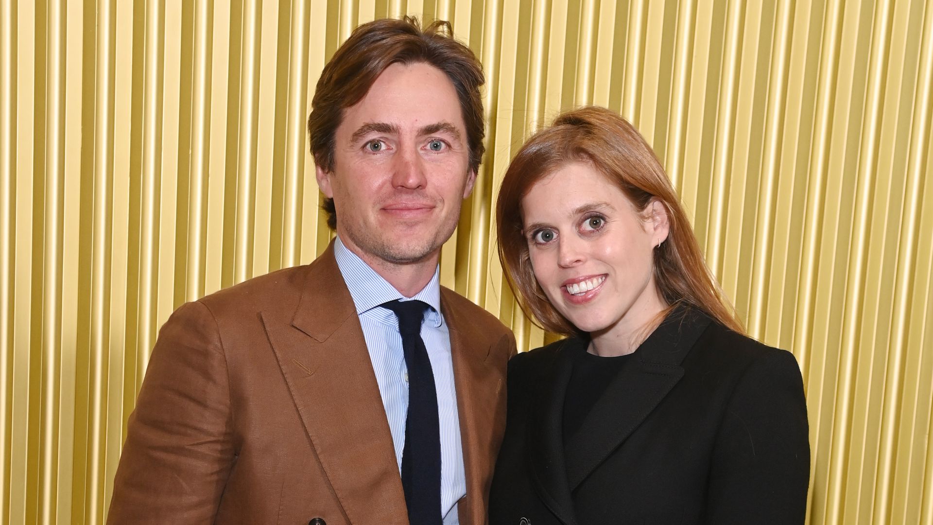 Princess Beatrice smiling in black dress with Edoardo in brown suit