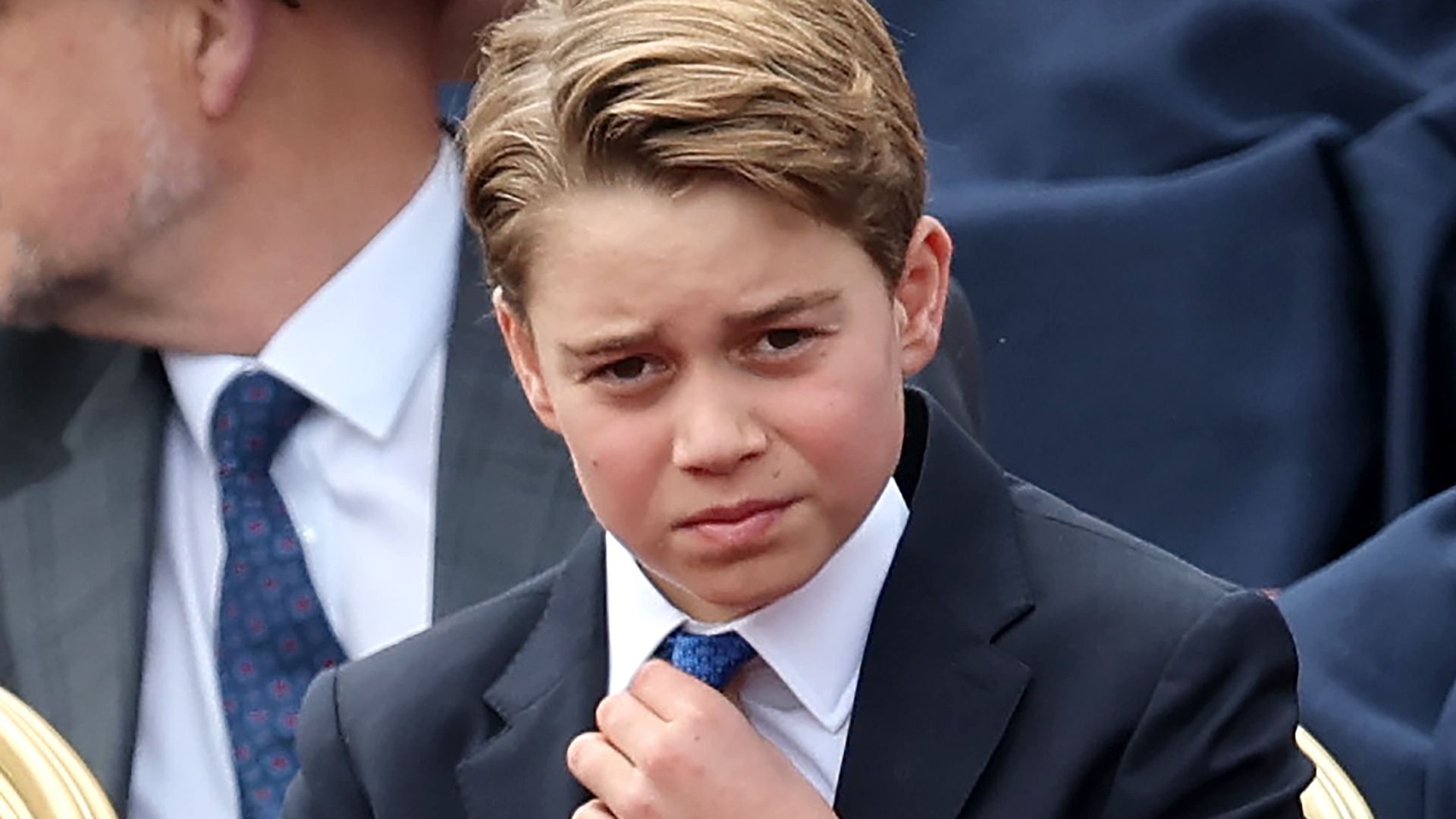 Prince George touching his blue tie and frowning