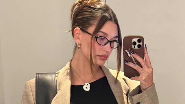 Hailey Bieber poses for a mirrir selfie in a blazer, black top and glasses