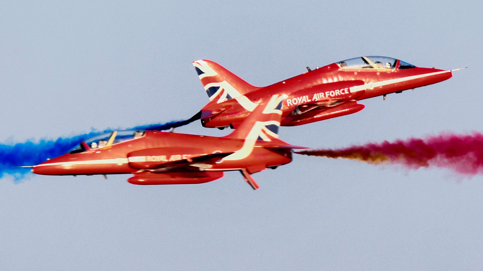 Two Red Arrows aircraft crisscross in the sky