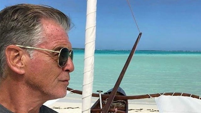 Pierce Brosnan in front of the sea and sand