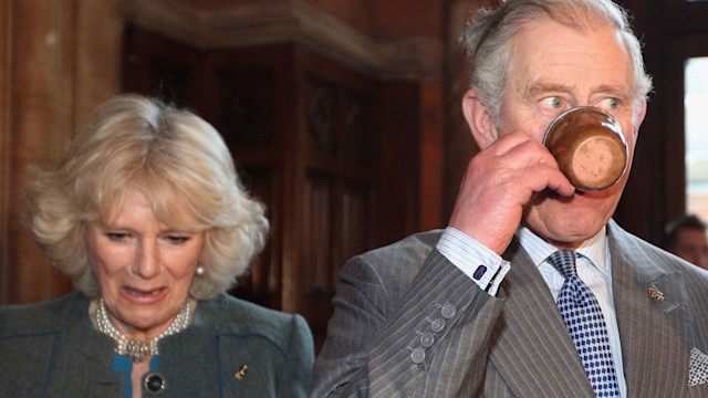 King Charles drinking out of a mug next to Queen Camilla