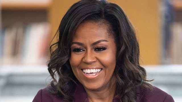 Michelle Obama in a maroon suit smiling with her hair in curls