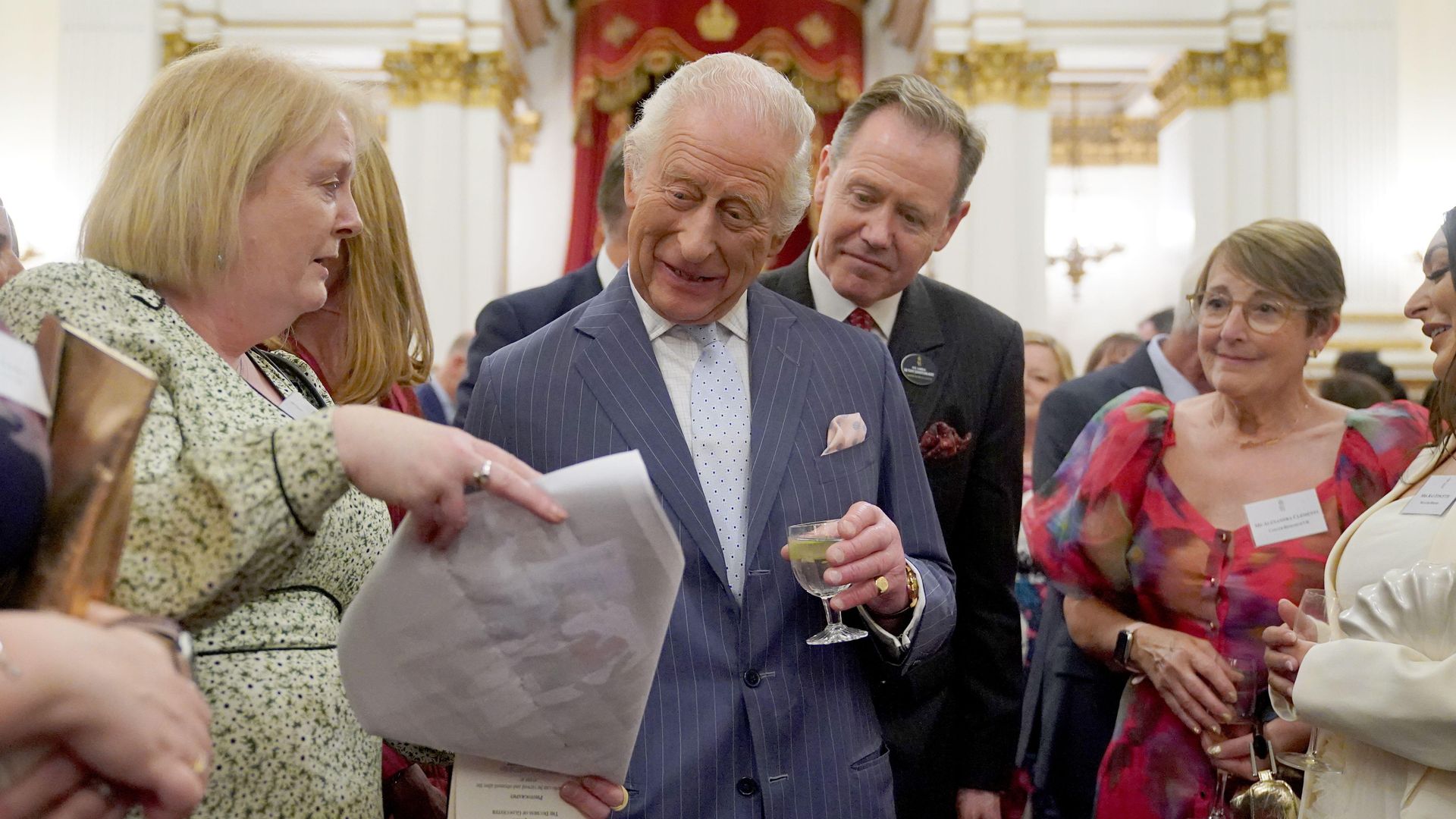 King Charles reading a large letter in a group of people