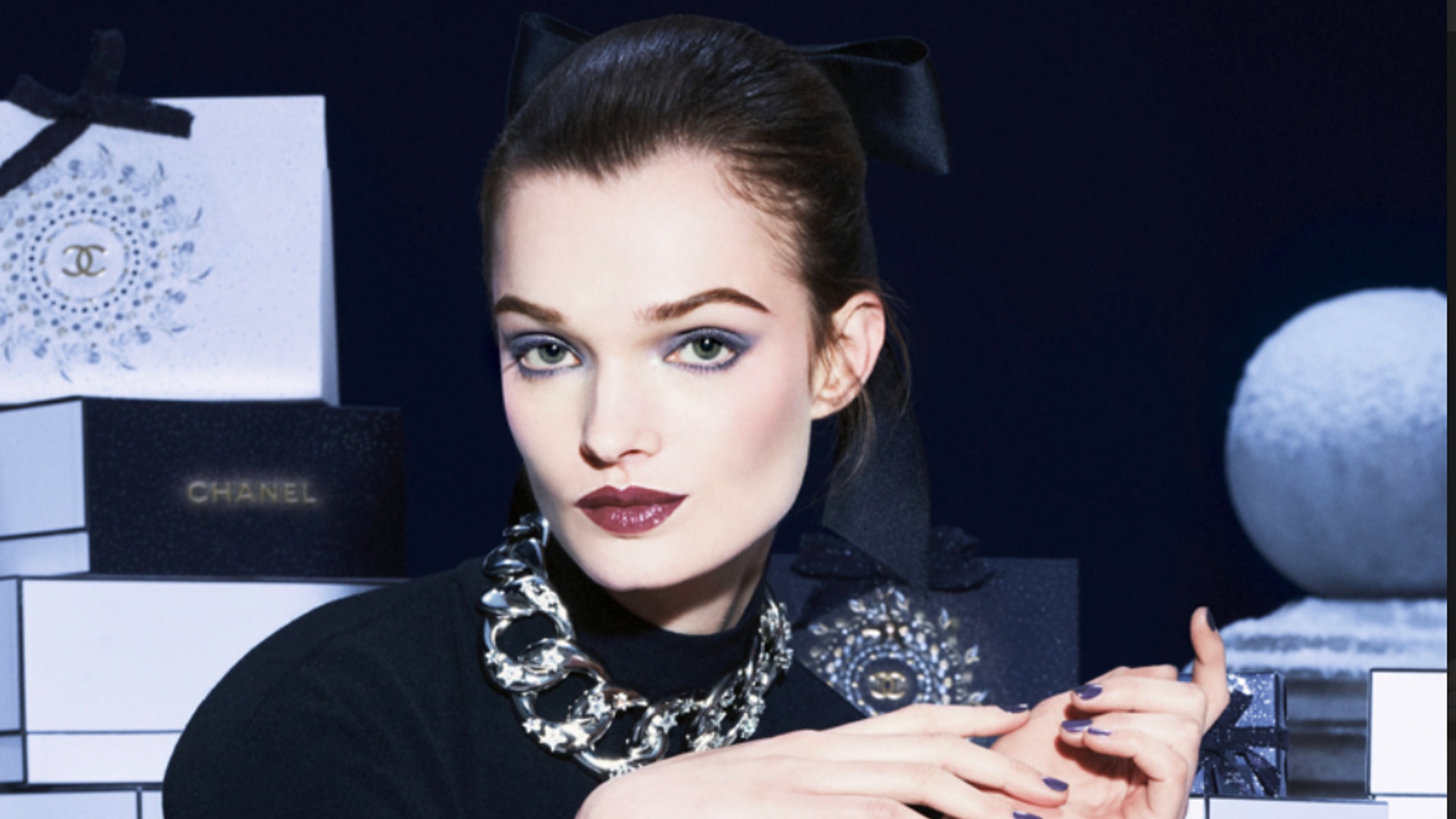 a model wearing a silver chain and surrounded by chanel bags 