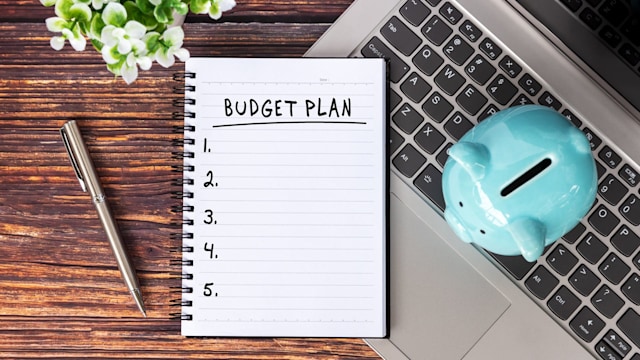 Budget Plan Text on Notepad next to laptop and piggy bank