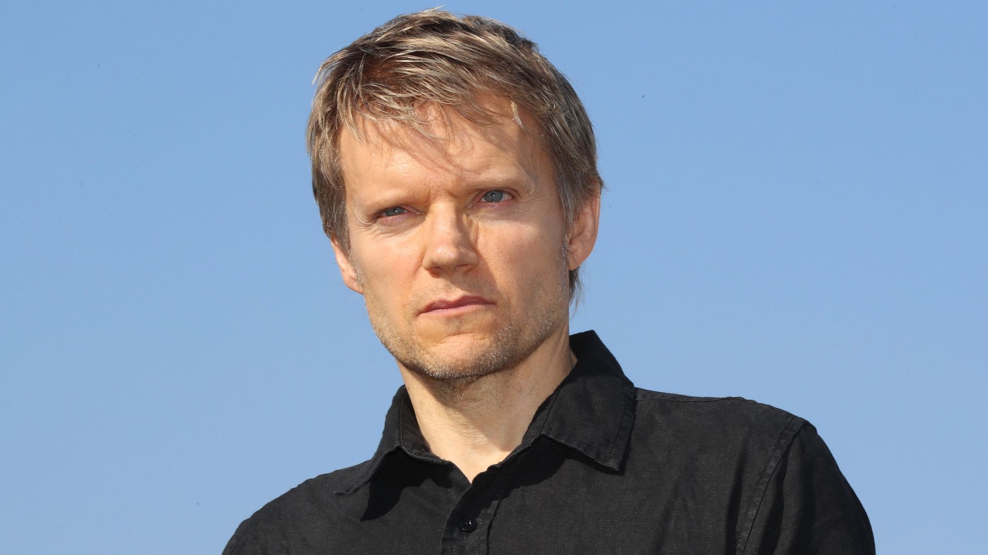 Marc Warren standing against a blue sky looking out ahead of the camera