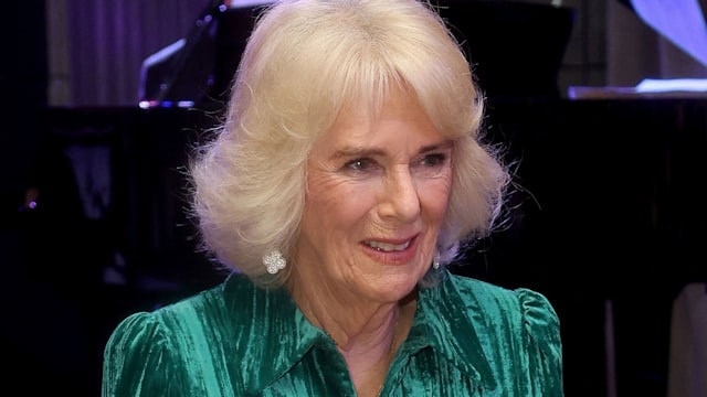 Britain's Queen Camilla in a green velvet dress holding a jumper