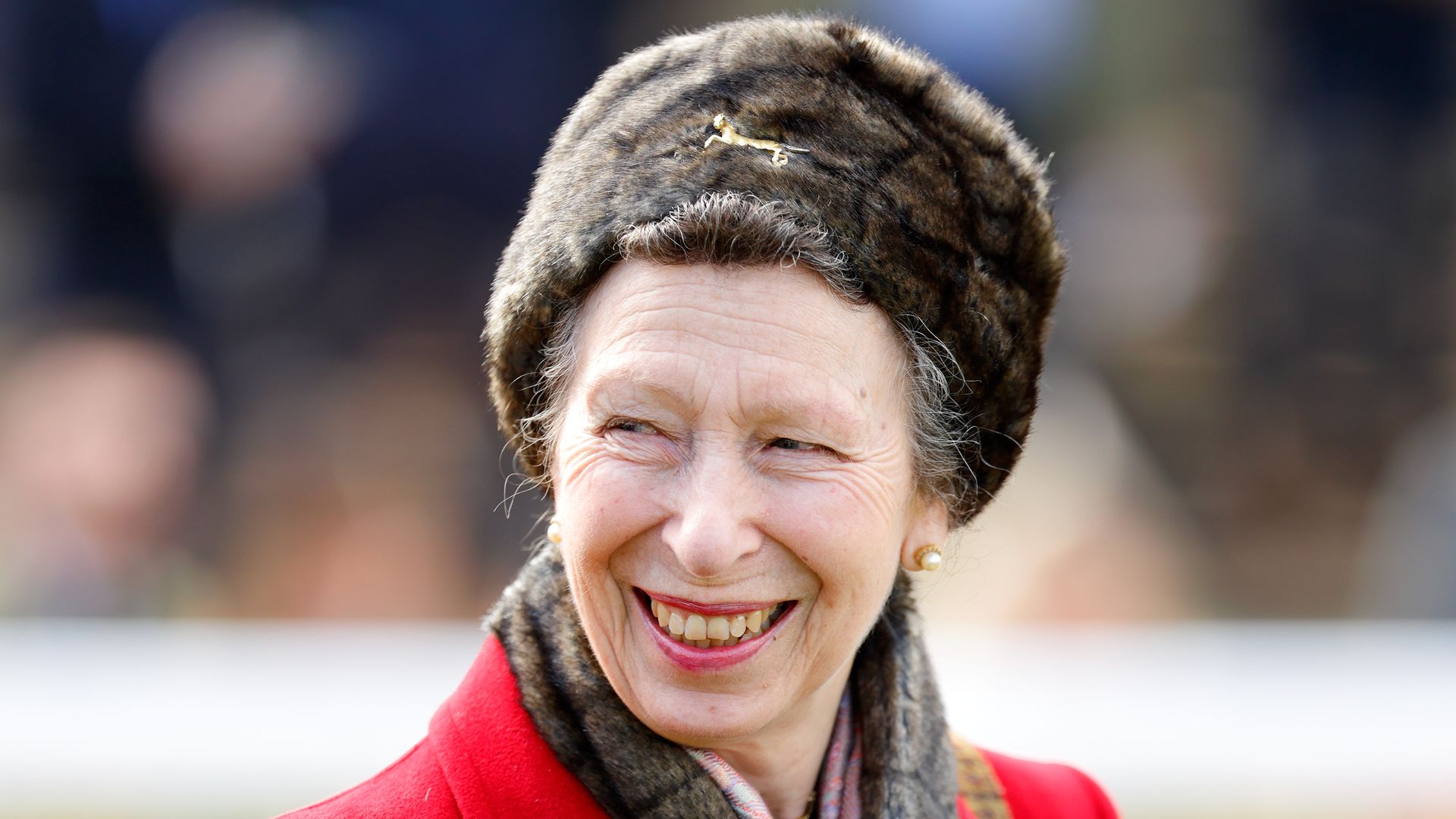 Princess Anne smiling in fur hat and red coat