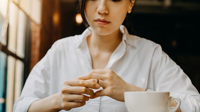 Woman touching the wedding ring on her finger nervously while having coffee and waiting in cafe