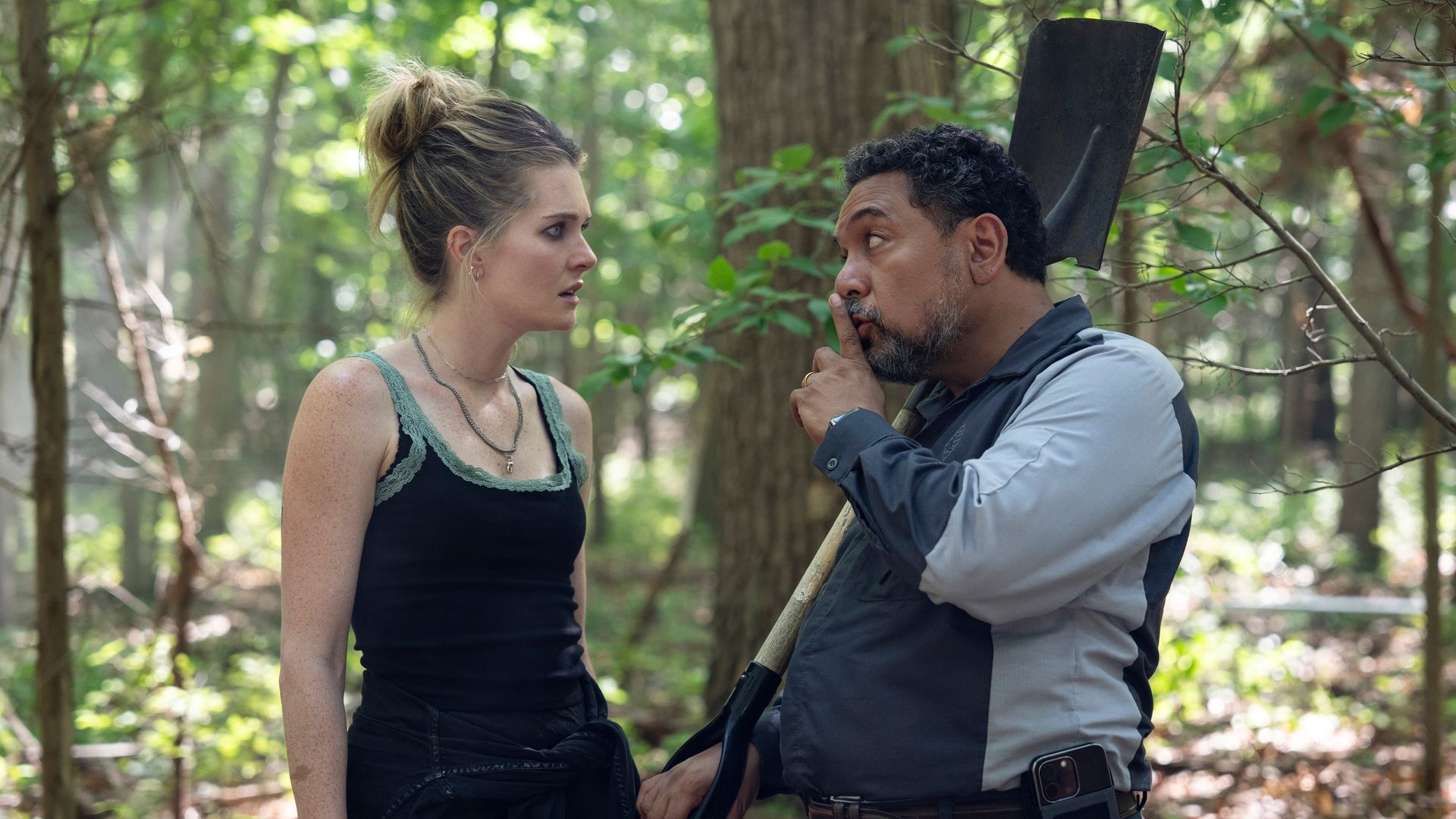 woman dressed in black and man holding shovel in woods
