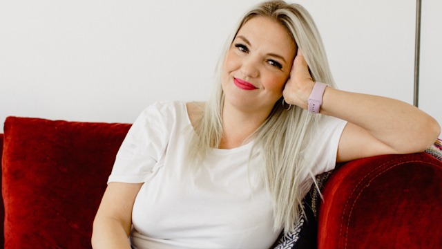 Blonde woman leaning her head on her hand on a red velvet sofa