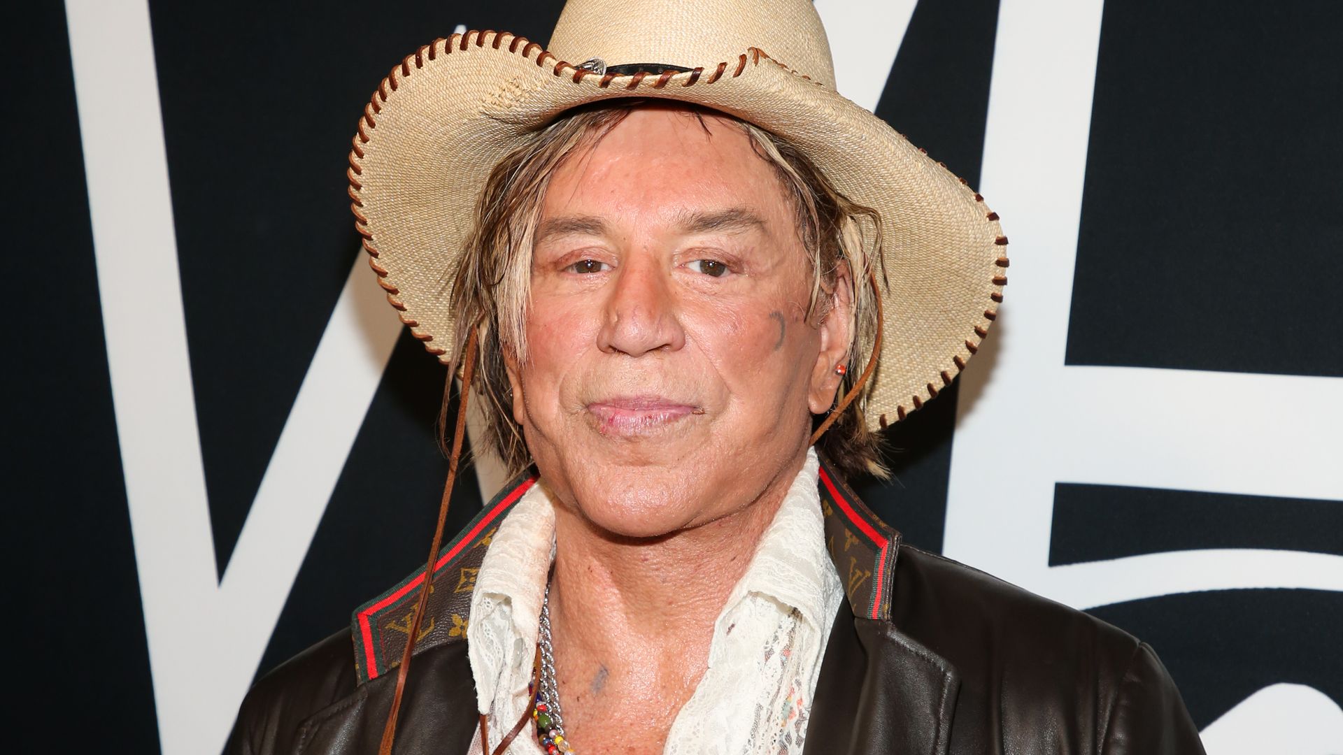 Mickey Rourke at red carpet event wearing a cream hat and brown leather jacket