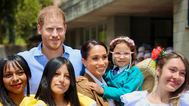 Meghan Markle and Prince Harry with a group of schoolchildren - Meghan is carrying a young girl