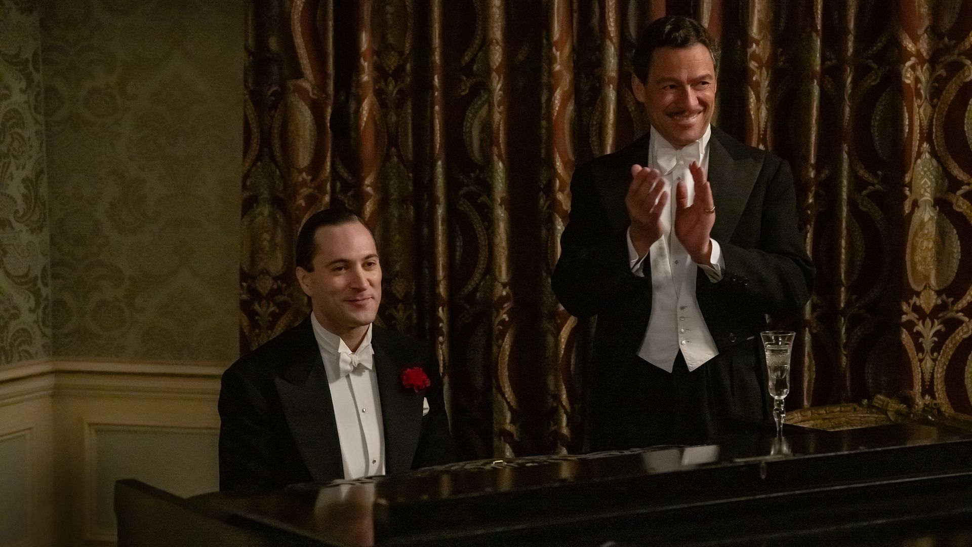 man in tuxedo playing piano, next to man standing in tuxedo