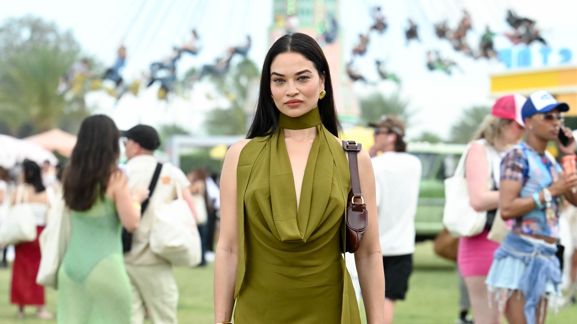 Shanina Shaik wears an olive green mini dress with a cowl neck and red cowboy boots at Coachella.