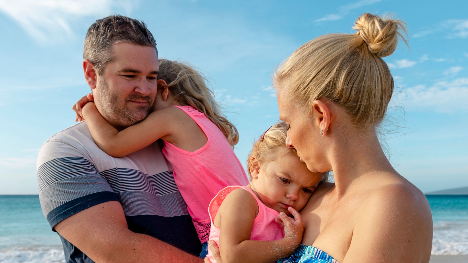 A shot of a caucasian family visiting the beach on a sunny day in Perth, Australia. They are smiling and embracing each other.