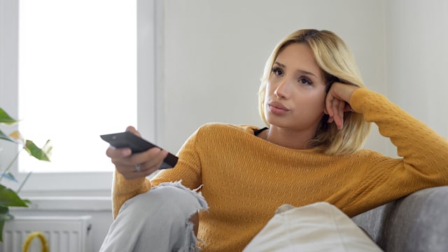 Bored woman holding tv remote control while sitting on a couch at home