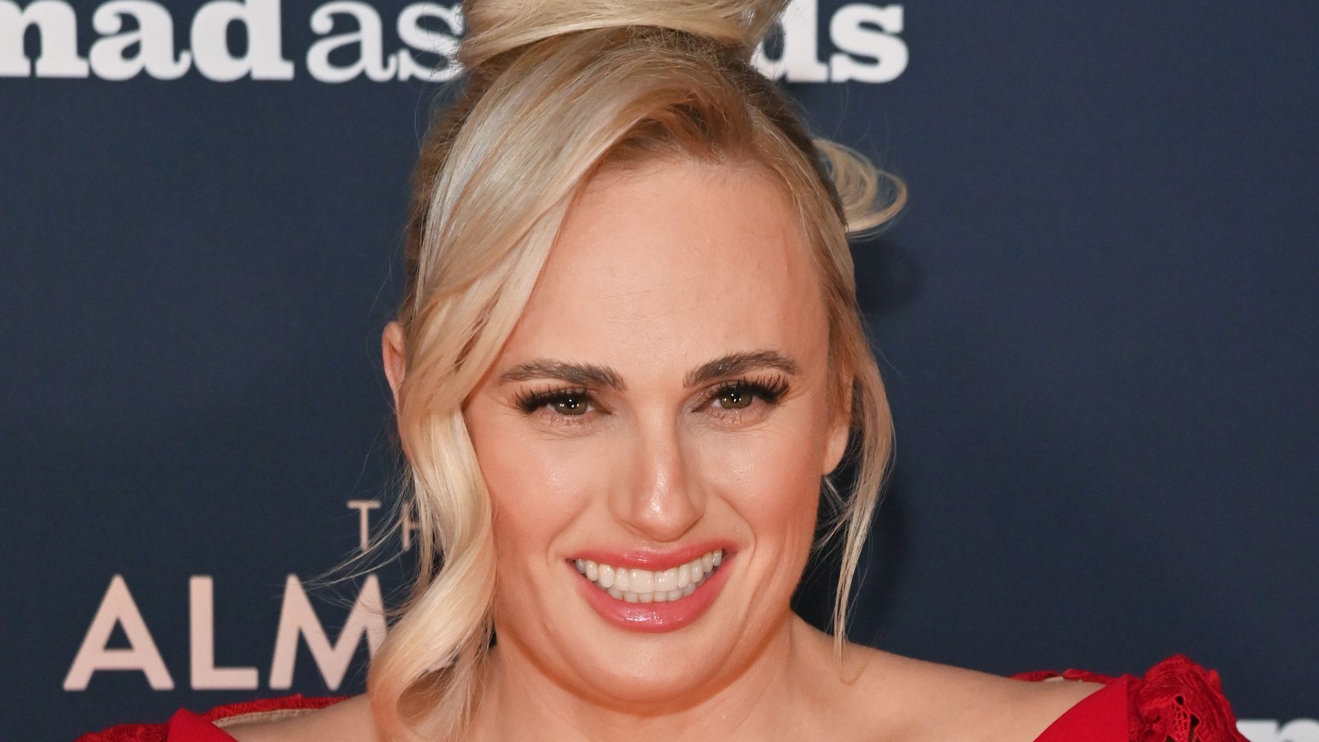 Rebel Wilson is a lady in red wearing sculpted lace gown