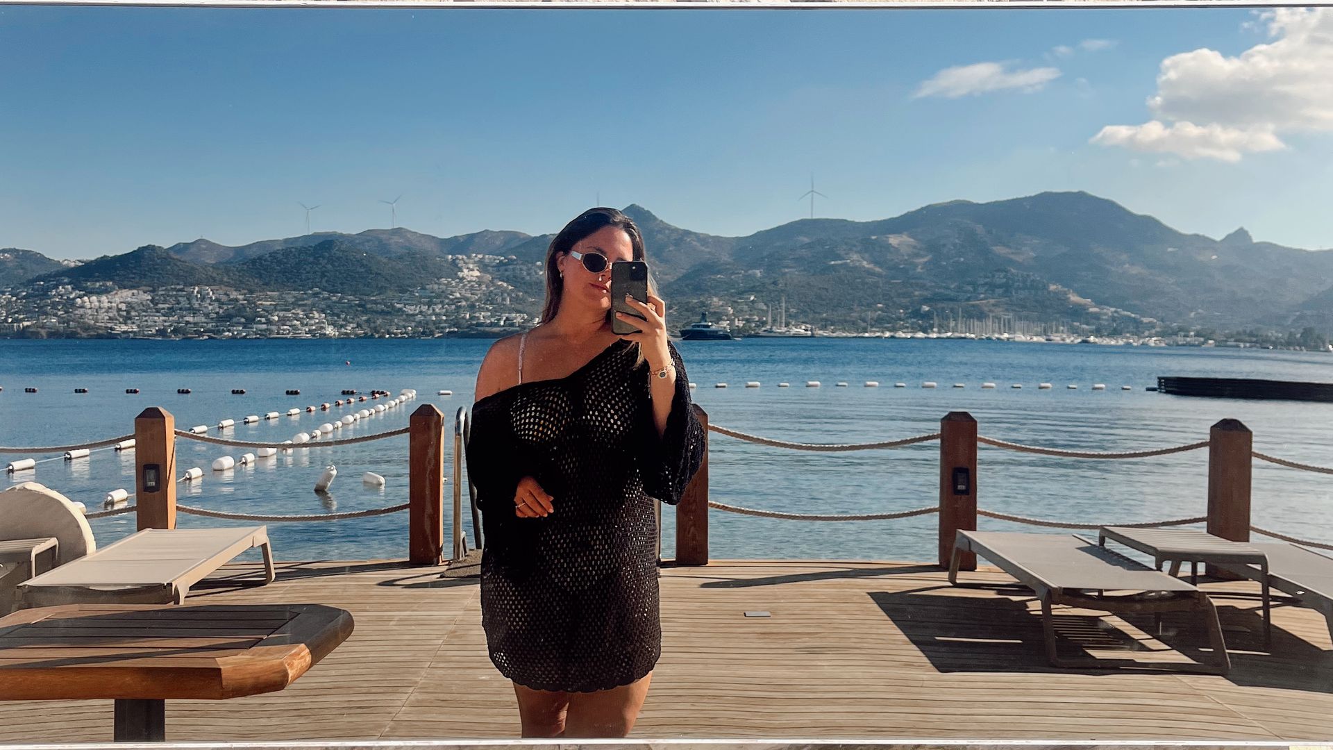 Invité prenant un selfie miroir sur la terrasse en bord de mer de l'Avantgarde Refined Bodrum, avec vue sur la baie et les montagnes de Yalıkavak.