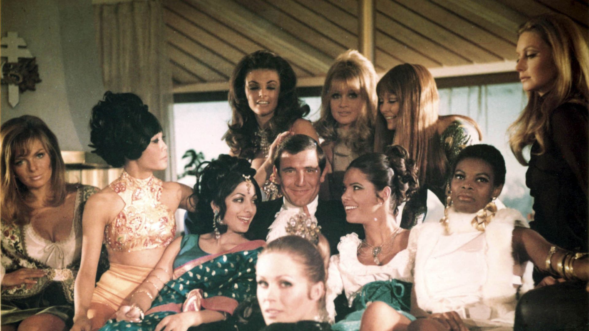 George Lazenby as James Bond surrounded by a group of women