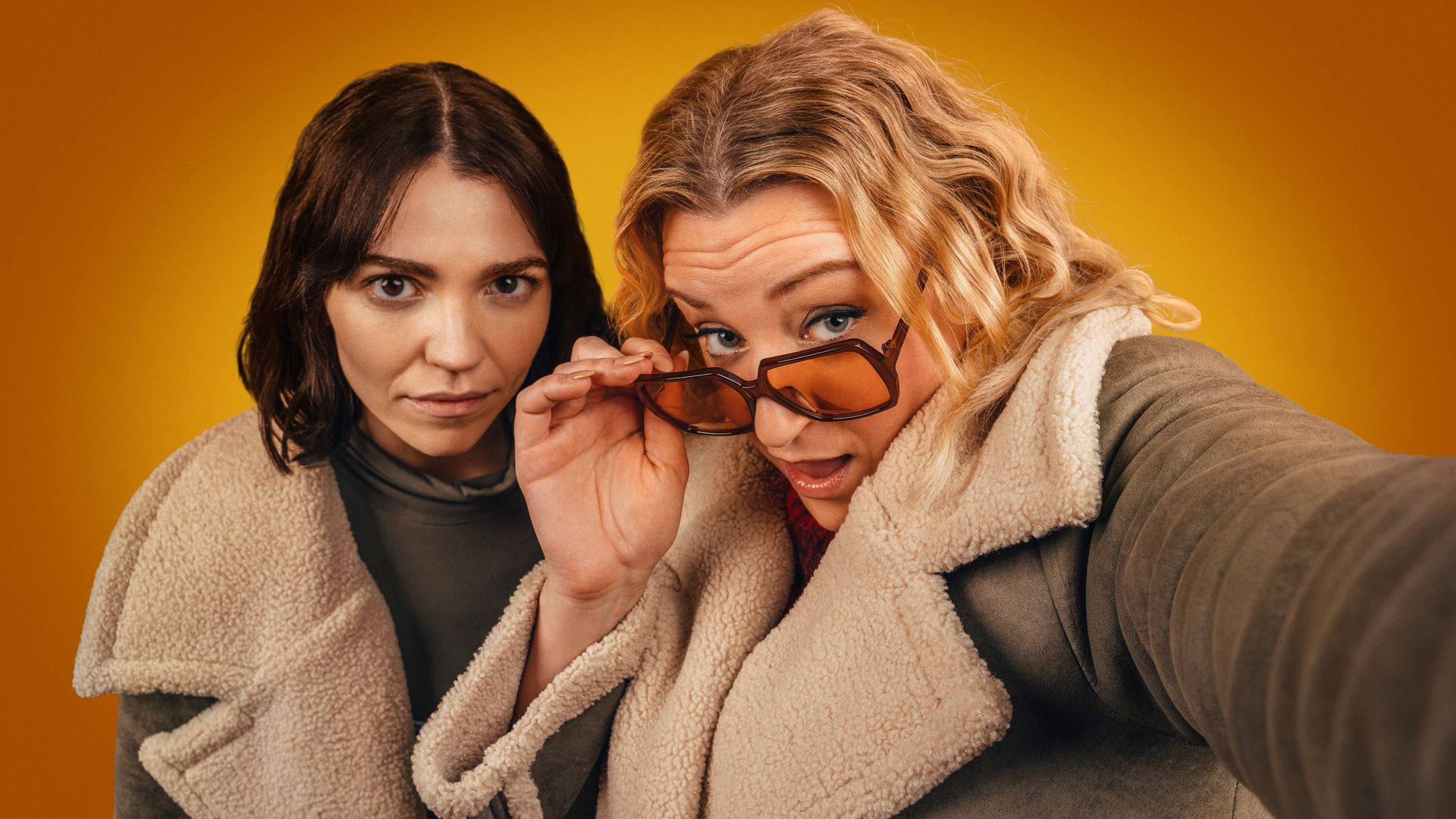 A brunette woman and blonde woman wearing glasses looking into camera