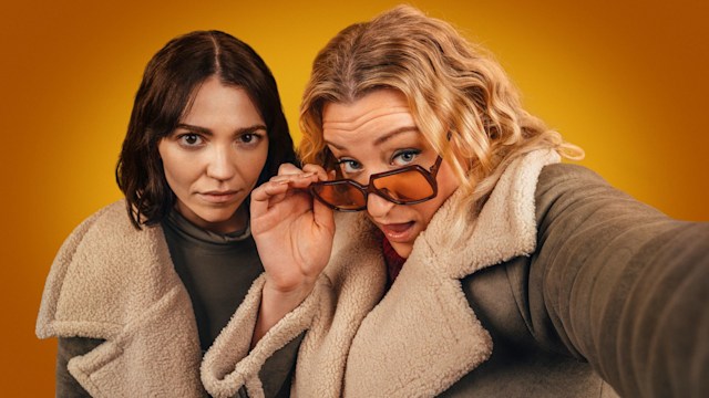A brunette woman and blonde woman wearing glasses looking into camera
