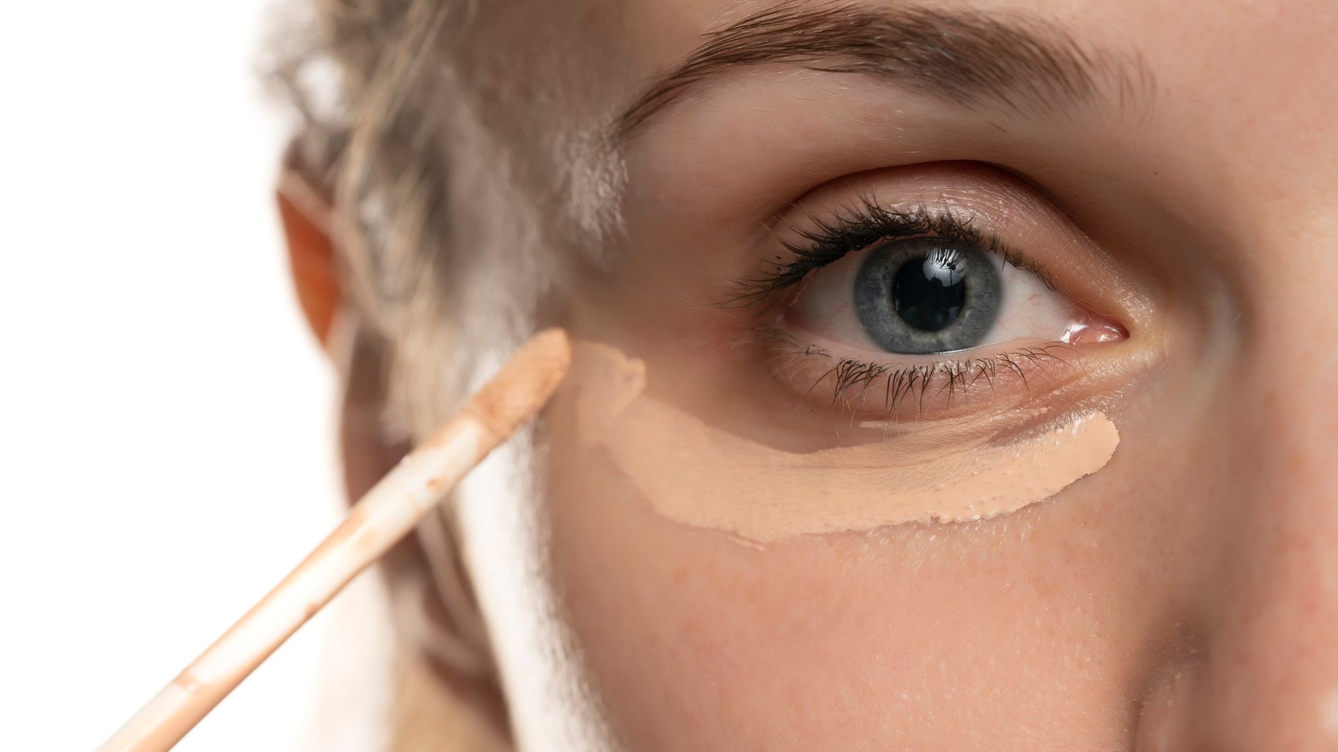 Closeup of a young woman applying concealer under her eye