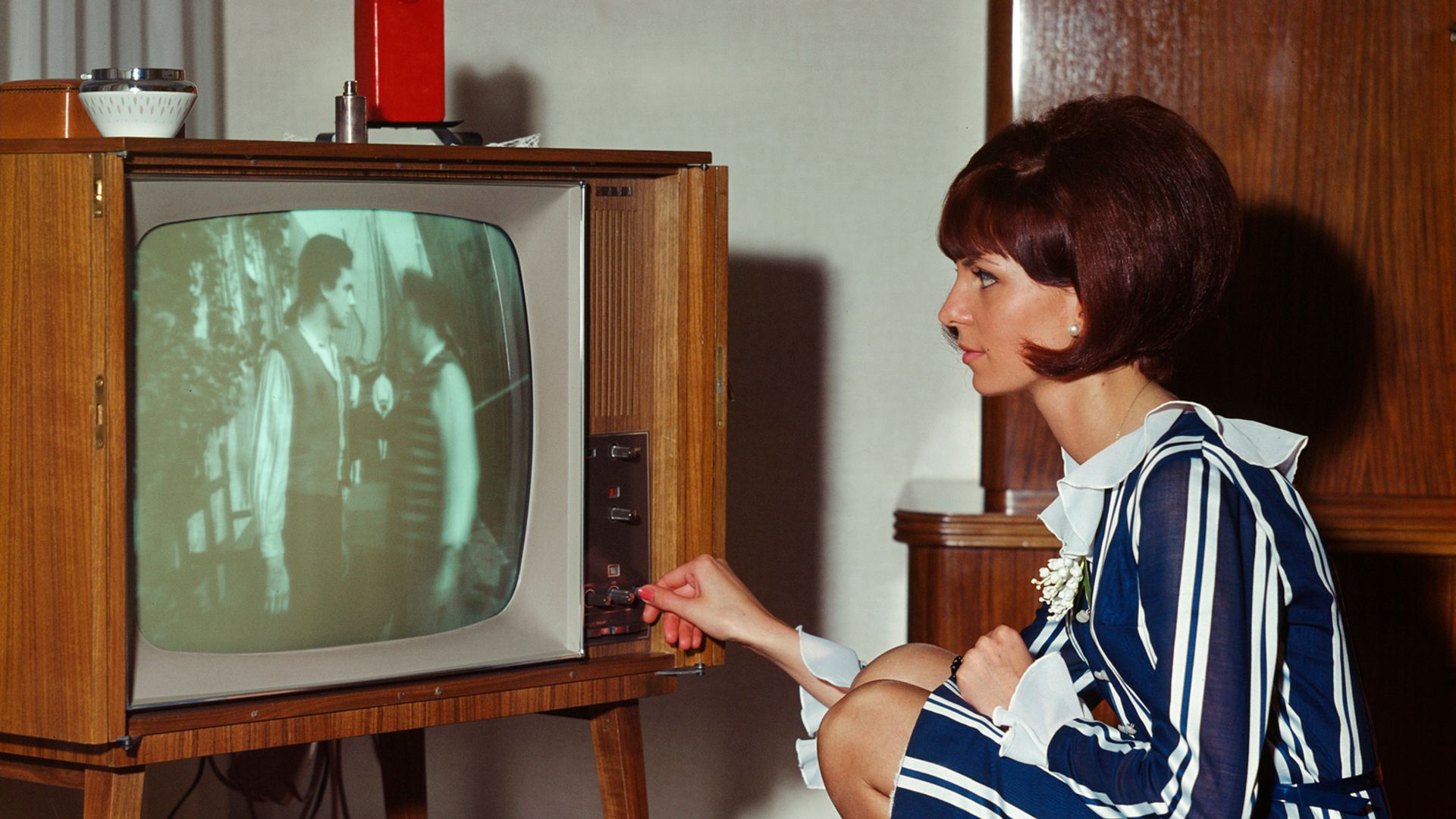 A Woman in a stripe dress crouched down watching retro television