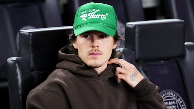 Cruz Beckham wearing a brown hoodie and bright green cap